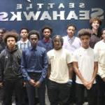 A large group of young men pose for a photo in front of a Seattle Seahawks sign